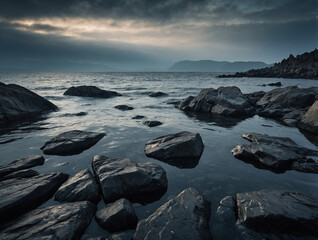 Fototapeta premium Smooth water surface reflecting a turbulent, textured sky, dark stone shoreline in sharp silhouette, layered composition with foreground boulders and distant ridge fading in haze.
