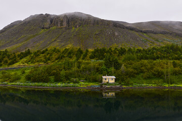 Fototapeta premium Small yellow house reflecting in a lake with green trees and mountain