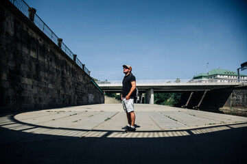 Man wearing cap and crossbody bag in sunny urban plaza