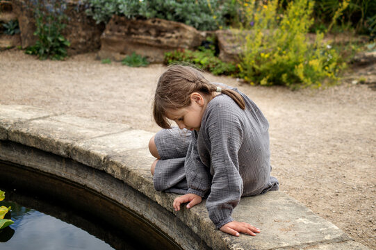 A young girl sitting at the edge of a pond in a botanical gardenю