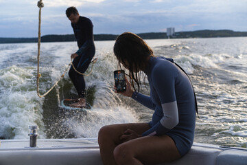 Man wake surfing on lake while woman films him during sunset