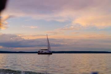 Sailboat drifting on calm lake under pastel sunset sky