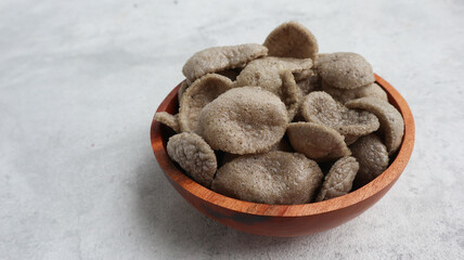 Kerupuk jengkol (jengkol crackers) is an Indonesian deep fried crackers made from starch, jengkol, and other ingredients that serve as flavouring. served on wooden bowel
