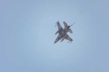 Fighter jet performing a steep banking maneuver in clear blue sky. Military fighter jet banking sharply during an aerial display against a bright blue sky.