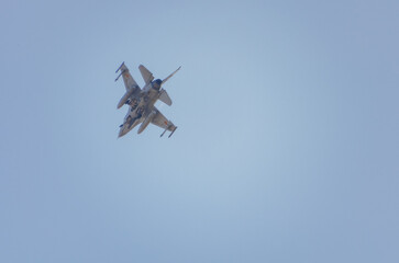 Fighter jet performing a steep banking maneuver in clear blue sky. Military fighter jet banking sharply during an aerial display against a bright blue sky.