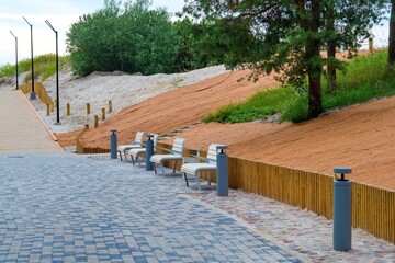 Modern coastal promenade with benches and lighting, next to reinforced sand dunes covered with...