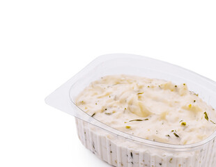 Creamy dip with herbs in a plastic container on a white background