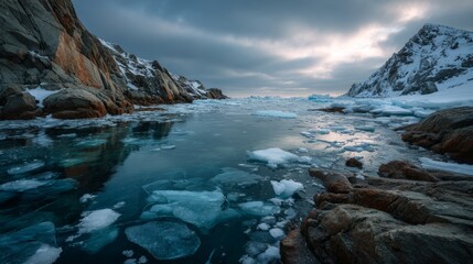 Obraz premium Dramatic winter seascape of rocky mountains reflected in partially frozen turquoise water under a cloudy twilight sky