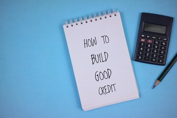 notebook with "HOW TO BUILD GOOD CREDIT" written on it with pencil and calculator isolated on blue background