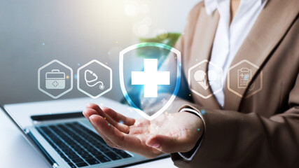 A businesswoman holds her hand under floating medical icons, including a shield with a cross, stethoscope, and heart. The image represents digital healthcare, health insurance, and medical technology.