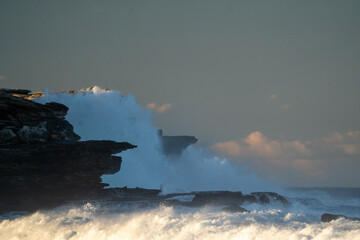 Waves at sunset crashing against cliffs, beach, dramatic light, vibrant colors