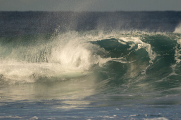 Ocean wave forming a small barrel, dynamic motion, blue water, natural surf, sunlight