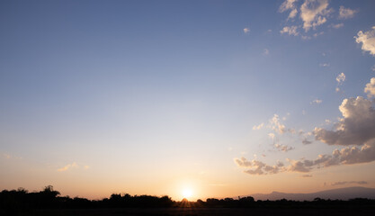 Sun sky and clouds at evening time in  horizontal composition. Blue orange and yellow color tone. Silhouette with mountain and forest. Suit for nature background.