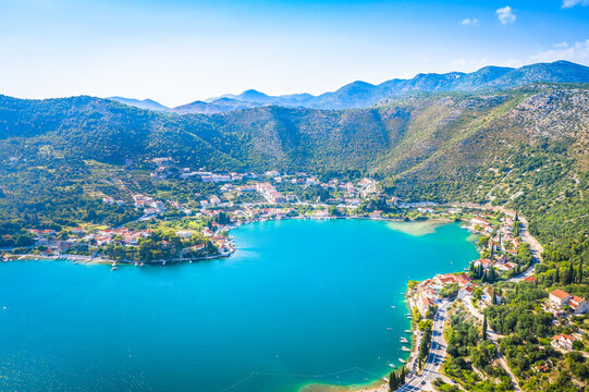 Drone photo of Zaton near Dubrovnik showing the entire bay with turquoise Adriatic waters, coastal houses, green hills, and a peaceful Mediterranean setting under clear sunny skies