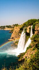 Coastal waterfall cascading into turquoise sea, rainbow visible