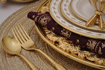 Closeup showing ornate gold cutlery, decorative charger plate, stacked fine china plates and patterned napkin arranged for formal dining, emphasizing luxury and elegance