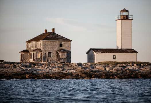 old lighthouse and living quarters sits on rocky island shore