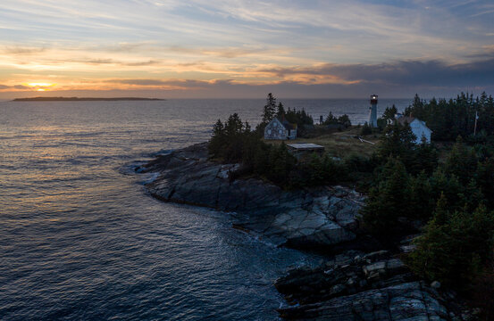 a lighthouse is perched at the edge of a rocky shoreline at sunset