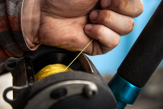 A fisherman holds yellow fishing line as he lets out slack from reel
