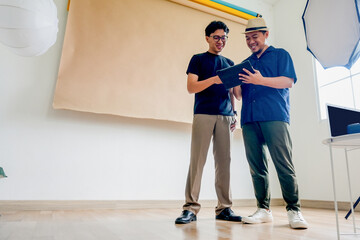Two Men Standing And Looking At A Tablet Screen While Discussing Ideas Before Photo Session
