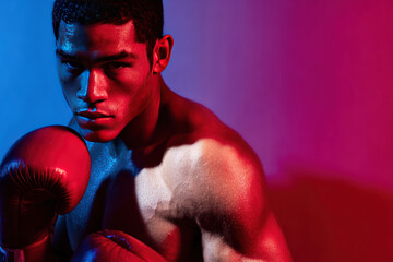 Boxer fighter young man with red boxing gloves in intense training pose under dramatic red and blue lighting, showing muscular upper body and focused expression