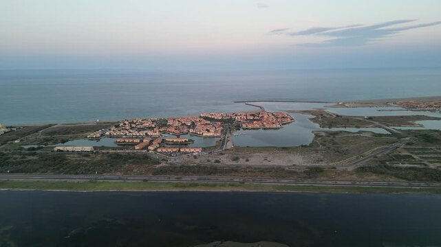 Aerial view of Etang de Leucate's buildings surrounded by water, reflecting sunset colors, as the tranquil sea meets the land, Etang de Leucate, Occitanie, France.