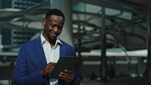 Portrait of African American investor makes online deals via tablet smiles in urban setting. Happy young businessman sells and buys cryptocurrency in business center. E commerce
