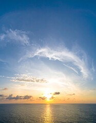 Wide panoramic sunset over calm ocean, with wispy clouds forming a halo around the sun