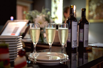 Champagne glasses on a bar with wine bottles in the background.