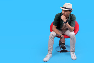 Stylish Male Photographer Sitting On A Red Chair, Holding A Camera Against and Put Hand on Chin