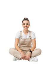 Young caucasian woman with brown hair in bun, white t-shirt, beige overalls, white sneakers, fitness tracker, red string bracelet, seated cross-legged on white studio floor, smiling at camera, with