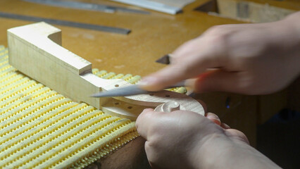 Skilled luthier carefully filing intricate violin scroll, highlighting meticulous craftsmanship and precision in stringed instrument creation