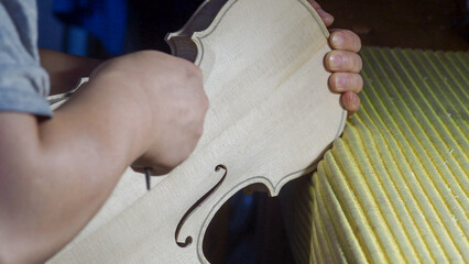 Skilled luthier carving violin soundboard with precision gouge, revealing intricate woodworking artistry in instrument crafting process