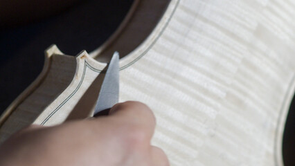 Skilled craftsman carefully carving violin body with specialized knife, revealing intricate woodworking technique and musical instrument crafting expertise