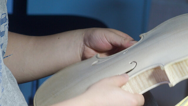 Close up of luthier's hands holding and inspecting unfinished violin part, showcasing the craftsmanship and precision involved in musical instrument making
