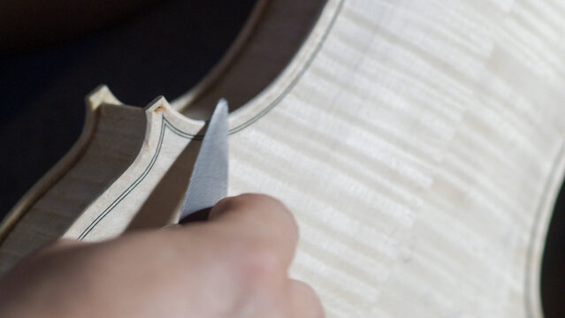 Skilled craftsman carefully carving violin body with specialized knife, revealing intricate woodworking technique and musical instrument crafting expertise