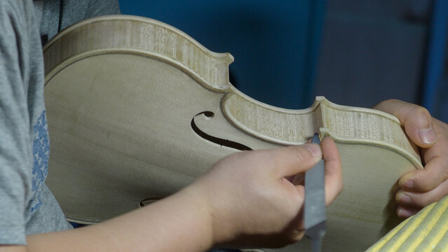 Skilled craftsman carefully filing violin soundboard, meticulously shaping wooden surface with specialized tool in traditional workshop setting - Powered by Adobe