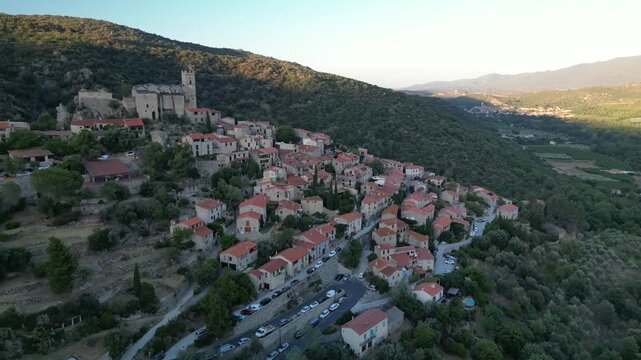 Aerial view of the medieval village of Eus with its castle nestled on the hillside, the red roofs contrasting with the green trees, Eus, Occitanie, France.