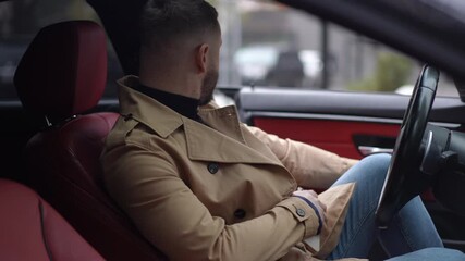 A stylish man in a fashionable trench coat sits in a car, making a phone call that reflects modern lifestyle - Powered by Adobe