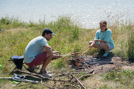 Caucasian couple roasting sausages over a fire. - Powered by Adobe