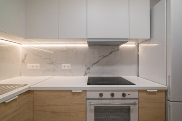 Modern kitchen with white cabinets, marble backsplash, and stainless steel appliances. Clean and minimalist design with bright lighting.