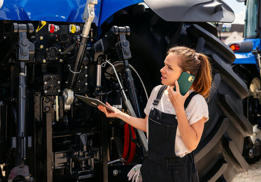 Confused female farm worker talking mobile phone near tractor at farm