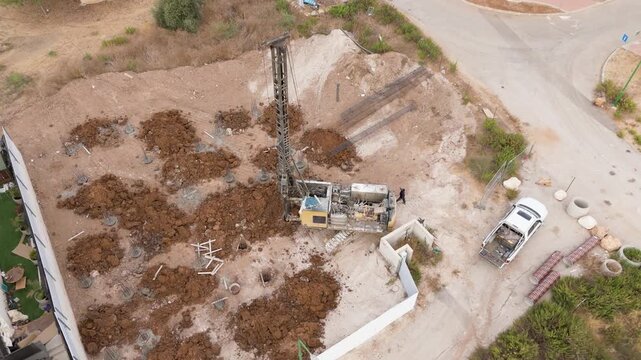 Sa'ar, Israel - 28 July 2025: Aerial view of a construction site, where a piling machine stands amidst heaps of dark soil, contrasting with the pale ground.