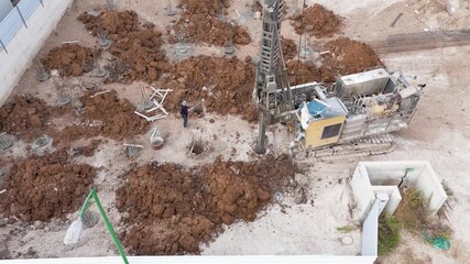 Sa'ar, Israel - 28 July 2025: Aerial view of a construction site with a drilling rig surrounded by mounds of earth and a worker standing near concrete foundations.