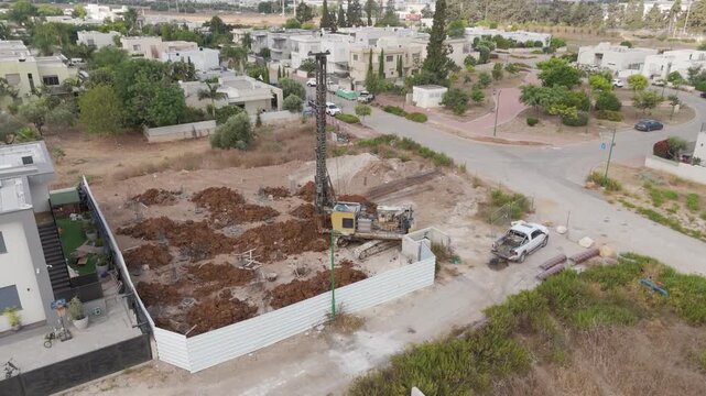 Sa'ar, Israel - 28 July 2025: Aerial view of a construction site with a drilling rig, surrounded by residential houses and green trees under the summer sky.