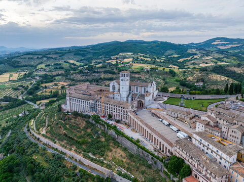 Aerial view of the Basilica of Saint Francis of Assisi standing majestically against a backdrop of rolling hills and verdant fields, Perugia, Umbria, Italy.