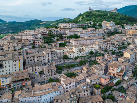Aerial view of sun-kissed rooftops cascade down the hillside, leading to the fortress atop Monte Subasio, a tapestry of history and nature, Perugia, Umbria, Italy.