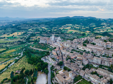 Aerial view of Basilica di San Francesco d'Assisi standing majestically amidst a tapestry of green hills and quaint rooftops, Assisi, Umbria, Italy.