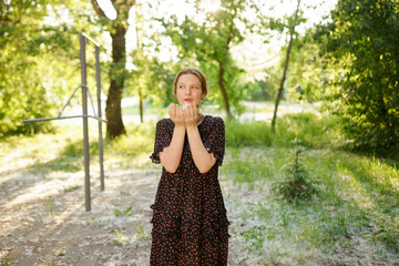 Smiling girl in black dress blowing poplar fluff outdoors in summer