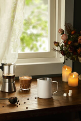 Cozy Morning Coffee Setup by the Window with Candles and Flowers, Coffee cup with milk and coffee beans on wooden table 
